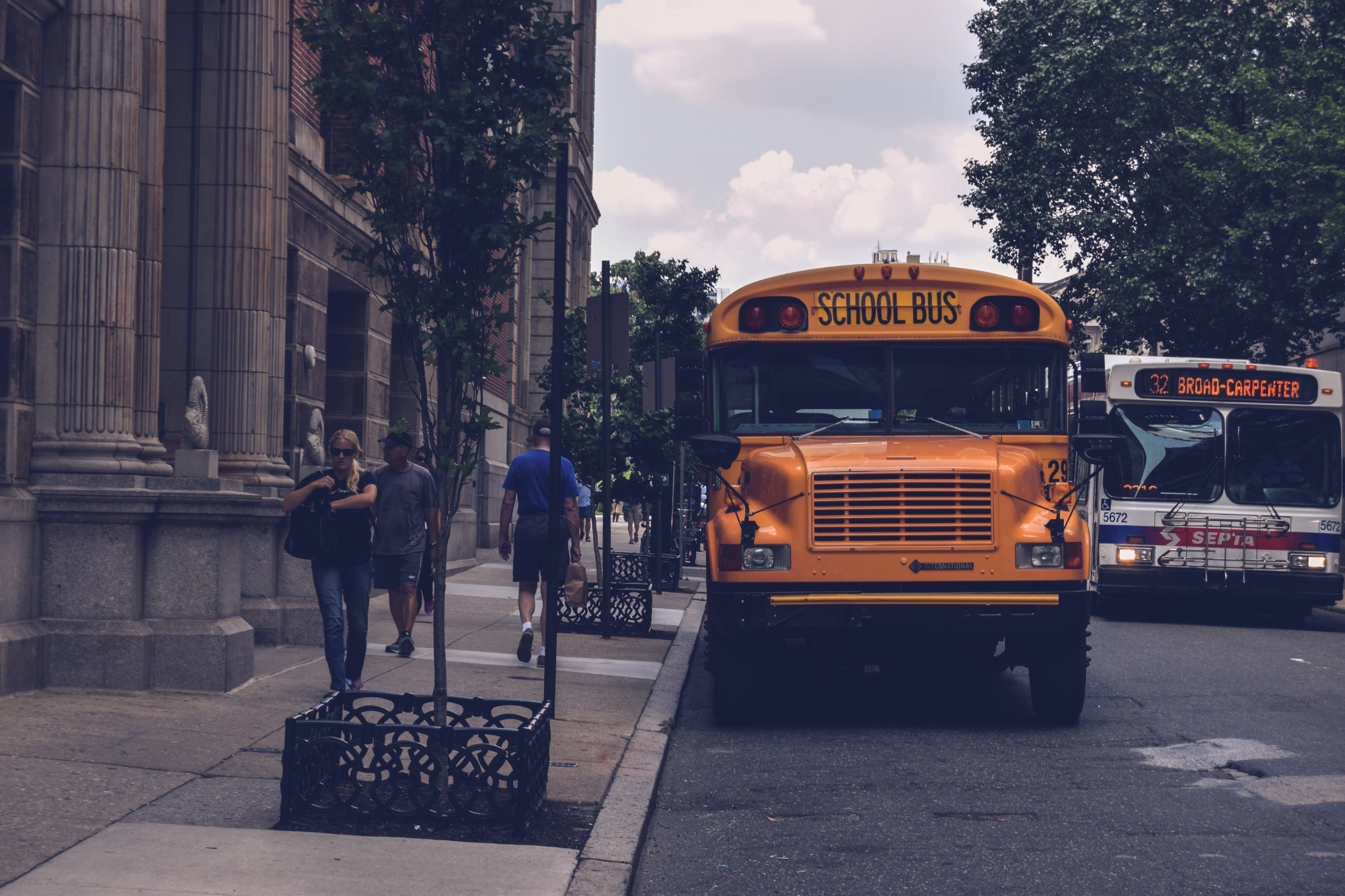 A yellow school bus parked in front of a school, with the building's entrance visible in the background.