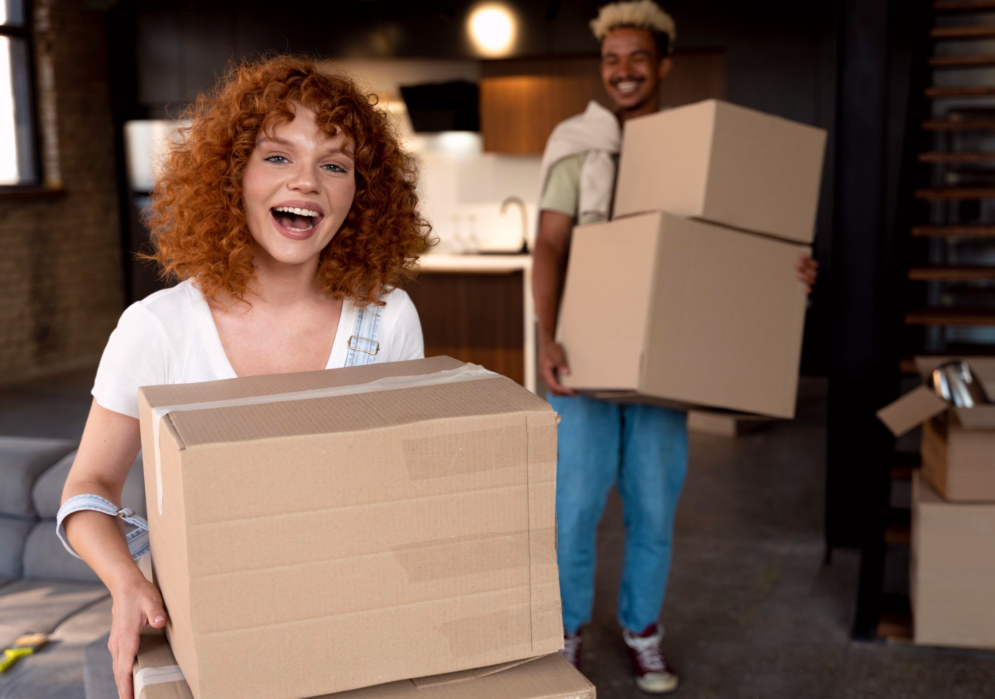 A happy couple holding cardboard boxes in front of their new home, ready to move in.