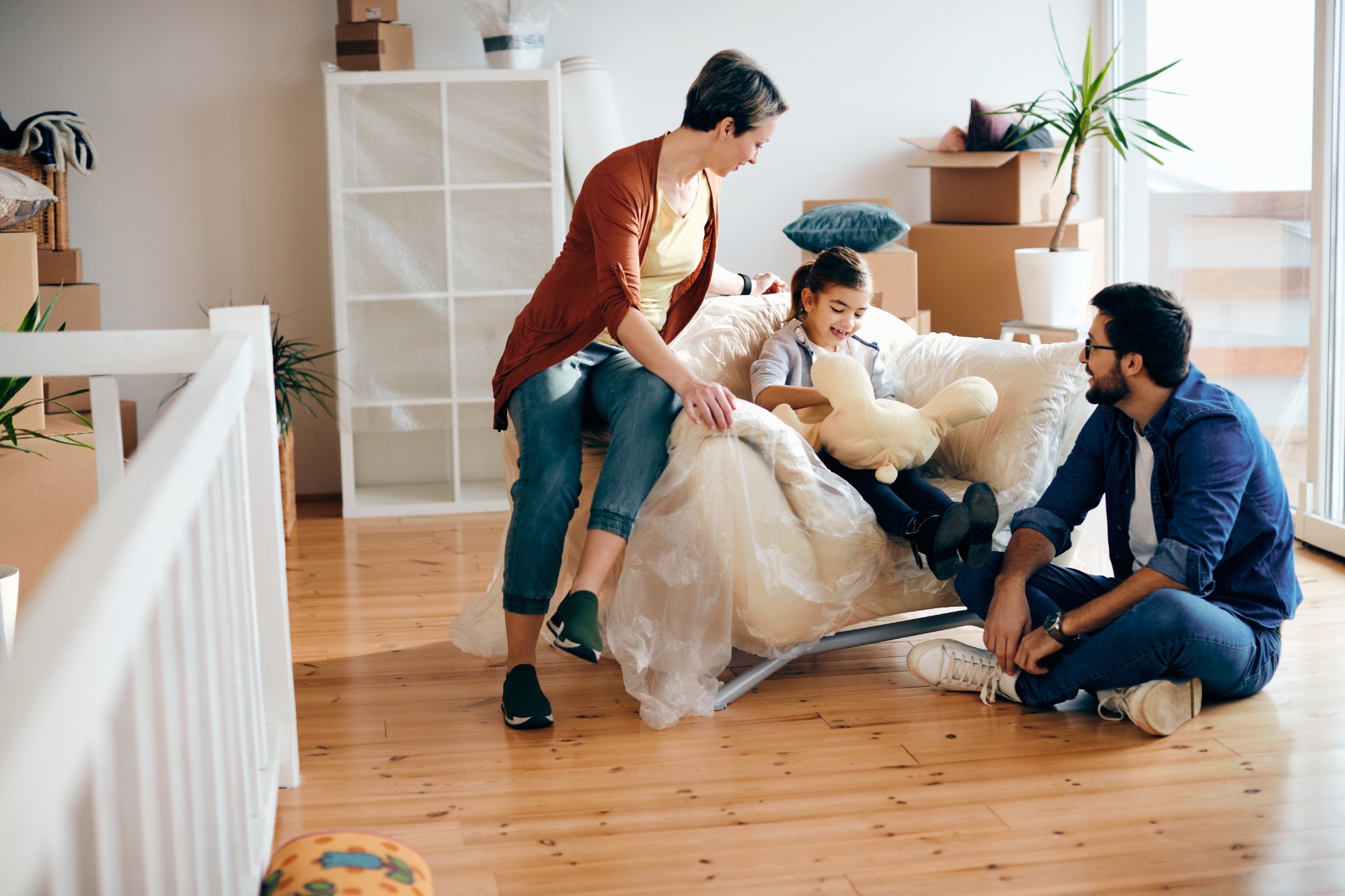 A happy little girl with her parents talking and smiling while carrying boxes into their new apartment.