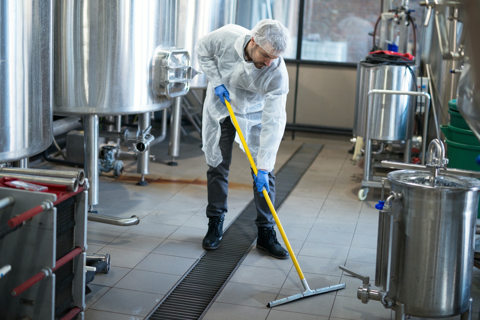 Professional cleaner in protective uniform meticulously cleaning the floor of a production plant.