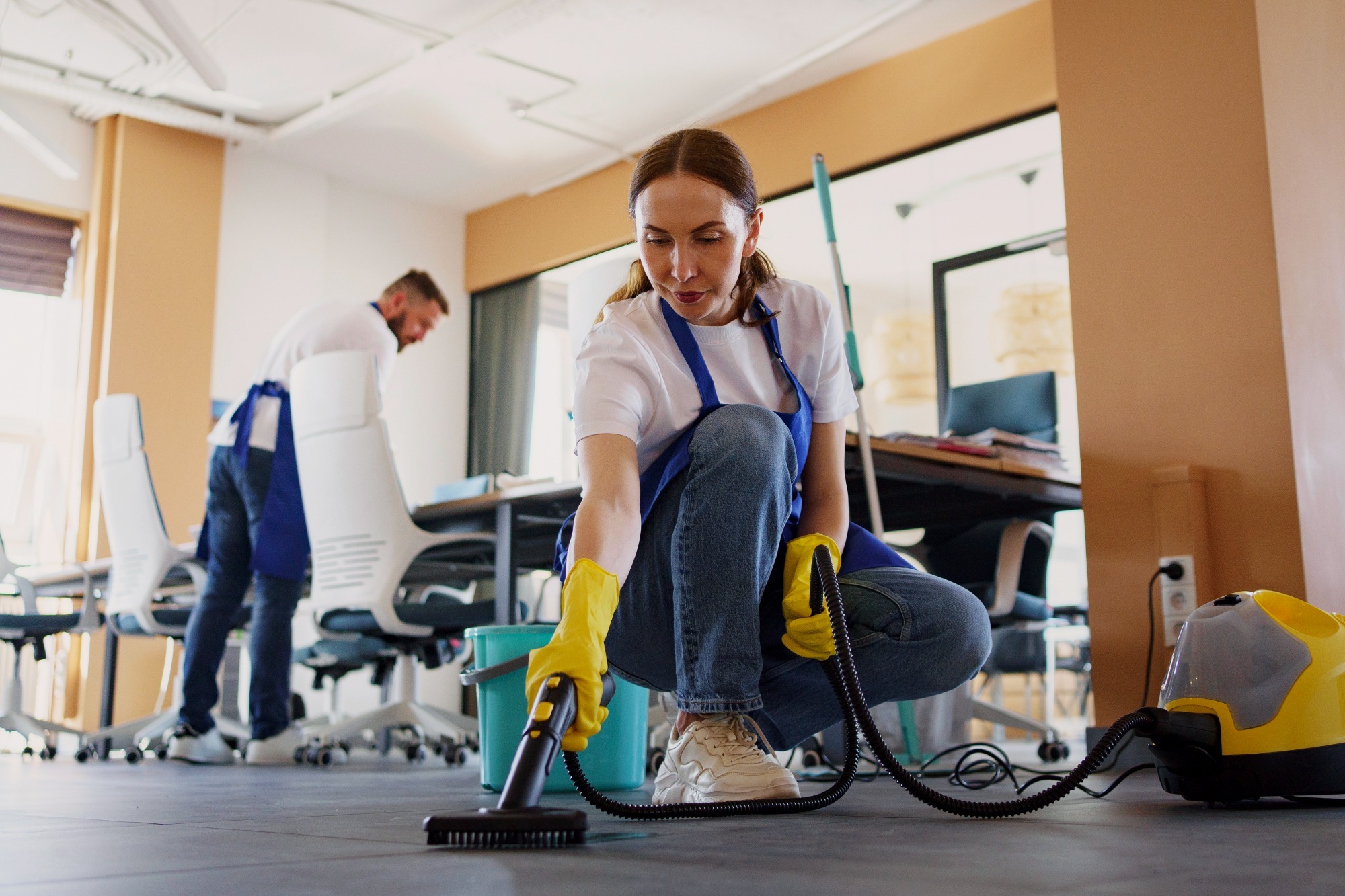 Maid vacuuming the floor in a well-lit office space.