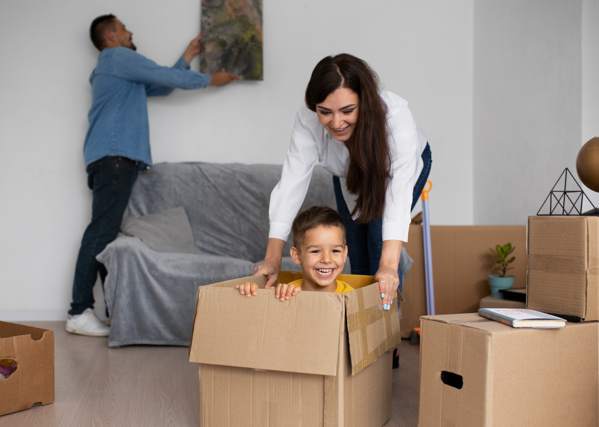 A happy family of three, including two parents and a child, holding boxes and smiling brightly as they stand in front of their new home, ready to move in