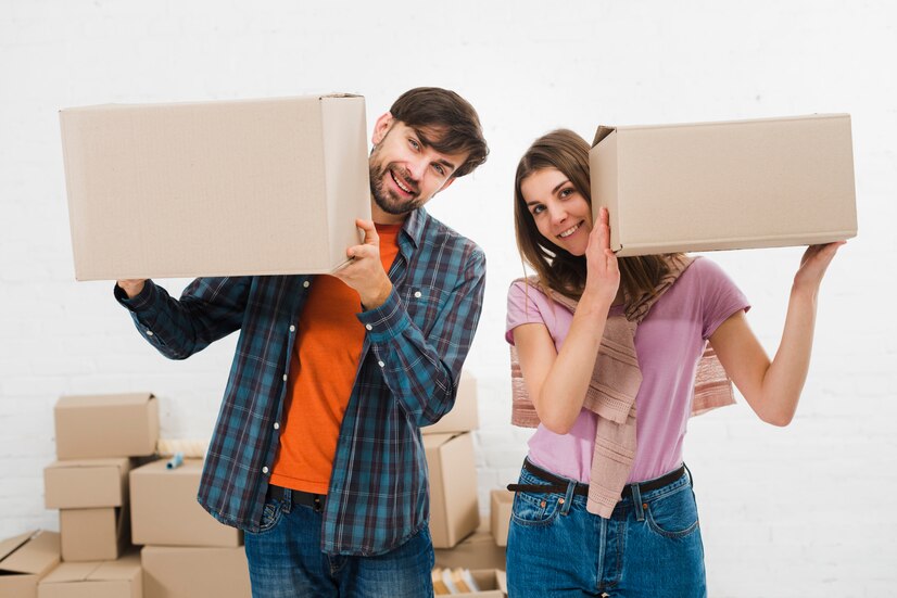 A happy couple holding moving boxes while smiling, ready to move into their new home in Providence.